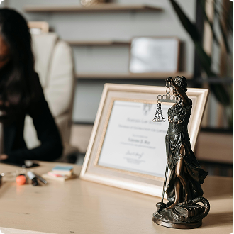 A bronze Lady Justice statue sits on a desk beside a framed certificate