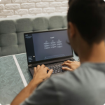 A person types on a laptop with a dark screen displaying text