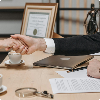 Two people shake hands across a wooden table with a laptop